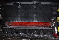 11_21450 Schmelzofen im Hydro Aluminiumwerk in Hamburg Finkenwerder - die Tr des Schmelzofens ist teilweise geffnet, das flssige Aluminium schimmert rotglhend durch den Spalt des Ofens. Ein Arbeiter mit  Schutzkleidung und Helm steht an der geffneten Ofenklappe und prft die Aluminiumschmelze. 