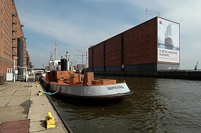 011_14778 ein Versorgungsschiff fr Trinkwasser liegt am Ponton - Schriftzug ' Hamburg ' am Heck; ein Transparent am Kaispeicher zeigt die zuknftige Architektur der Elbphilharmonie. 