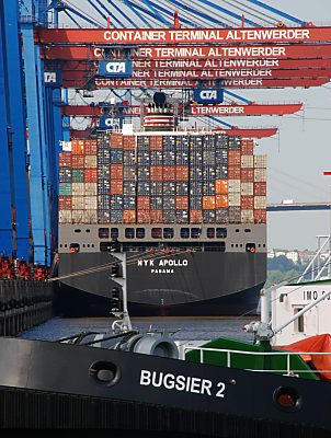 011_15593 - das Heck eines Container- schiffs; die bunten Container sind in sieben Lagen gestapelt - im Vordergrund Detail des Schleppers BUGSIER 2.