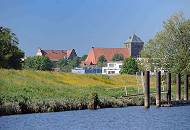 073_4791 Blick vom Flusslauf der Schwinge zur Stadt Stade; alte Eisenpoller am Ufer der Schwinge zeugen von dem ehemaligen Wirtschaftsverkehr, der auf der Fluss stattgefunden hat. Am Deich des Flusses bl�hen gelbe Blumen - im Hintergrund die dreischiffige gotische Hallenkirche St. Wilhadi.