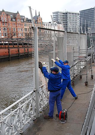 011_17383 - ein zweiter Arbeiter sichert die grossen Gitterteile des Zollzauns direkt an der Kaimauer des Zollkanals - im Hintergrund die Jungfernbrcke. Fotografie