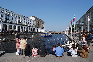 011_15624 - Touristen sitzen am Wasserrand und geniessen den Ausblick; andere fttern Schwne; in der Bildmitte fhrt das Polizeiboot der Alster. 