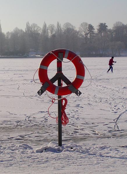 275_1010026 Ein Rettungsring hngt am Ufer des Stadtpark Sees im Schnee - das Wasser ist zugefroren und mit hohem Schnee bedeckt. Ein Skilanglufer berquert den See bei seinem Lauf durch den Hamburger Stadtpark.