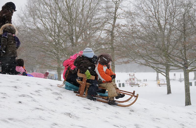 Fotos vom Hamburg im Winter - Kinder rodeln im Winterhuder Stadtpark. 276_5027 Im dichten Schneetreiben lassen sich die Kinder ihren Spass nicht nehmen, einen kleinen Hgel im Hamburger Stadtpark herunter zu rodeln. Im Hintergrund der Spielplatz und das eingeschneite Planschbecken.