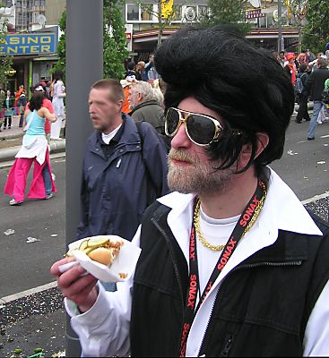 011_14215 - ein brtiger Elvis mit Goldkette und grosser Sonnenbrille mit Goldrand isst ein Sandwich am Spielbudenplatz.