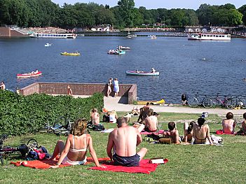 011_14536 - Freizeit in Hamburg: Menschen sitzen in Badehose und Bikini auf der Wiese am See und blicken auf die Kanus und Alsterschiffe, die auf dem Stadtparksee wenden und wieder Richtung Alster fahren werden.