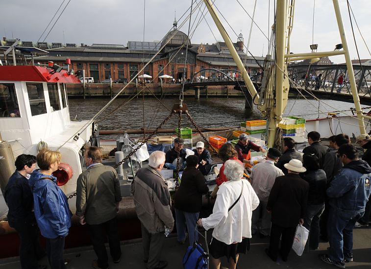 Bilder der Hamburger Sehenswrdigkeiten  - Fischkutter, Fischverkauf St. Pauli Fischmarkt  33_47906 Am Anleger Altonaer Fischmarkt hat der Cuxhavener Fischkutter ELVSTINT am Sonntag Morgen fest gemacht. Direkt vom Kutter verkauft die Besatzung die frisch gefangenen Fische auf dem Fischmarkt an ihre Kunden. Im Hintergrund das restaurierte historische Gebude der Altonaer Fischauktionshalle, das jetzt als Hamburger Eventlocation / Veranstaltungsort dient.  www.fotos-hamburg.de