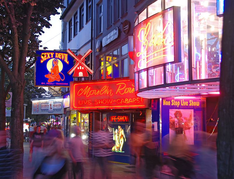 Hamburgbilder von den Sehenswrdigkeiten der Hansestadt. Kietz auf St. Pauli. Leuchtwerbung an den Gebuden der Reeperbahn - Reklame fr Live Show + Cabaret.Hamburg-Fotografie Christoph U. Bellin.  34_41203 Fr Hamburg Touristen ist die Reeperbahn der Ausgangspunkt fr den Besuch des Hamburger Rotlichtviertels. Die Werbetafeln leuchten im Abendhimmel und laden zum Besuch der Live Show im Moulin Rouge ein. Passanten schlendern ber die Sndige Meile, dem Kietz von Hamburg St. Pauli.