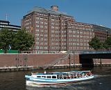 33_47953 Eine Barkasse der Hamburger Hafenrundfahrt fhrt mit Touristen an Bord am Rande der Hamburger Speicherstadt auf dem Zollkanal; das Schiff hat gerade die Wand- rahmbrcke passiert. Seitenansicht der Backsteinarchitektur des Messberghofs, lks. ein Ausschnitt vom Chilehaus mit der Hamburg Fahne auf dem Dach. www.fotograf-hamburg.de