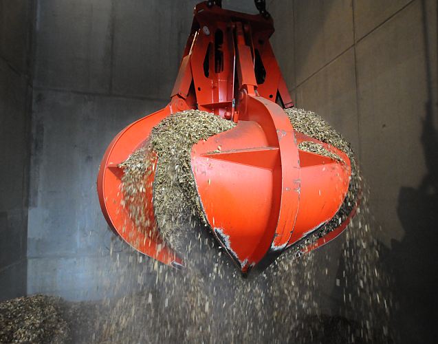 Fotografie Holzheizkraftwerk - Transport Holzspne mit dem Greifer.  33_48023 Der Greifer nimmt die Holzspne nach der Anlieferung auf und transportiert seine Fracht in das hohe Silo in dem der Rohstoff fr die Energiegewinnung gelagert wird.  Tglich liefern ca. 5 - 7 Lastwagen das geschredderte Holz an. Fr die geplanten 50 - 60 Millionen Kilowattstunden im Jahr an erzeugter Wrme und 13 Millionen Kilowattstunden Strom werden ca. 30.000 Tonnen naturbelassenes Holz bentigt. Dies soll aus der Landschaftspflege kommen wie z. B. zerkleinertes Knickholz oder im Frhling beschnittene Bume, deren sten dann im Holzschredder zerkleinert werden. www.fotograf-hamburg.com