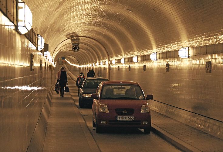 Bilder von Hamburg - KFZ und Fussgnger in der Tunnelrhre Alter Elbtunnel  33_48038 Fr Fussgnger und Radfahrer ist die Benutzung kostenfrei; auch die Unterquerung der Elbe ist zeitlich nicht eingeschrnkt. Fr Kraftfahrzeuge muss eine Nutzungsgebhr bezahlt werden und die Durchfahrt ist nur werktags, Montag bis Freitag von 5:30 bis 20:00 Uhr mglich. Der St. Pauli Elbtunnel wurde 1911 erffnet und gilt als Meisterleistung der Ingenieurskunst; ca. 4400 Arbeitskrfte arbeiteten fast vier Jahre an den beiden 426m langen Tunnelrhren. Auf zwei Fahrbahnen knnen Fussgnger und PKW die Elbe in 24m Tiefe unterqueren - Fahrsthle transportieren die Autos und Menschen hinunter.  www.bilder- hamburg.de