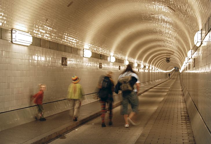 Hamburger Sehenswrdigkeiten - Alter Elbtunnel, Fussgnger in der Tunnelrhre  33_48042 Fr Fussgnger und Radfahrer ist die Benutzung des Alten Elbtunnels kostenfrei; auch die Unterquerung der Elbe ist zeitlich nicht eingeschrnkt. Fr Kraftfahrzeuge muss eine Nutzungsgebhr bezahlt werden und die Durchfahrt ist nur werktags, Montag bis Freitag von 5:30 bis 20:00 Uhr mglich. Der St. Pauli Elbtunnel wurde 1911 erffnet und gilt als Meisterleistung der Ingenieurskunst; ca. 4400 Arbeitskrfte arbeiteten fast vier Jahre an den beiden 426m langen Tunnelrhren. Seit 2004 steht die Anlage des Tunnels unter Denkmalschutz. Auf zwei Fahrbahnen knnen Fussgnger und PKW die Elbe in 24m Tiefe unterqueren - Fahrsthle transportieren die Autos und Menschen hinunter.  www.bilder-hamburg.de