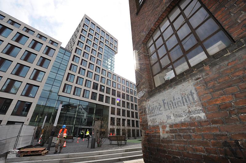 Hamburg-Fotos; Architektur in der Hamburger Innnenstadt; Brahmsquartier - Gängeviertel. Moderne Architektur des Brahms Quartiers + Backsteinmauer eines Gebäudes des Gängeviertel Hamburg. 17_1949 Das Brahmsquartier ist 2009 fertig gestellt worden - Bauarbeiter mit Signalweste gehen über den Platz auf dem die Brahmsstele steht. Rechts eine Backsteinwand eines der historischen Industriearchitektur im Hambuger Gängeviertel. Ein altes handgeschriebenes Schild an der Mauer " Keine Einfahrt - Die Finanz-Deputation".