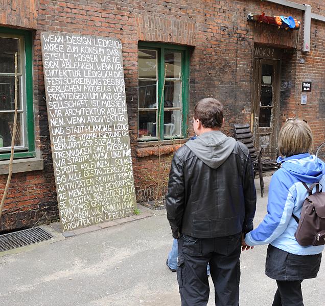 Bilder Hamburg - Hinterhof im Hamburger Gngeviertel.Widerstand gegen den Abriss + Sanierung.  21_1941 Besucher des Gngeviertels lesen eine Tafel ber Konsum und Architektur. Seit dem 22. August 2009 besetzten ca. 200 Knstler das Gngeviertel und fordern sowohl Raum fr Kreative als auch den kompletten Erhalt der historischen Gebude. Diese Initiative namens Komm in die Gnge will „ein selbstverwaltetes, ffentliches und lebendiges Quartier mit kulturellen und sozialen Nutzungen“ schaffen.