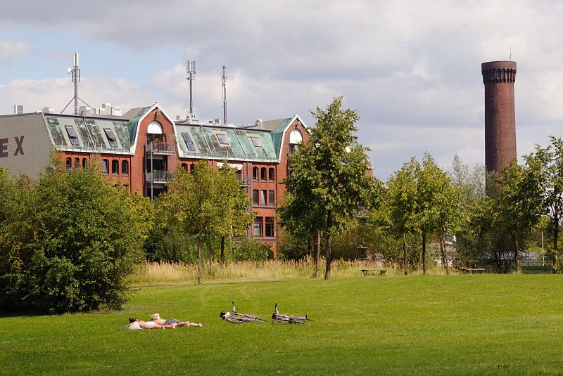 Elbpark Entenwerder; Gruenanlage in Rothenburgsort - Speichergebude, Wasserturm. Historische Architektur Hamburgs Spreicher Industriegebaeude Gruenderzeit.  1453_3695 Die Grnanlage Entenwerder Elbpark ist 1997 fertig gestellt worden und befindet sich auf dem Areal der ehmaligen Zollstation Entenwerder mit den angegliederten Hafenanlagen. Zwei Frauen sonnen sich auf der Wiese des Parks, die Fahrrder liegen auf dem Boden. Im Hintergrund der Turm der Wasserkunst von Rothenburgsort und die Industriearchitektur eines historischen Fabrikgebudes / Speichergebudes.