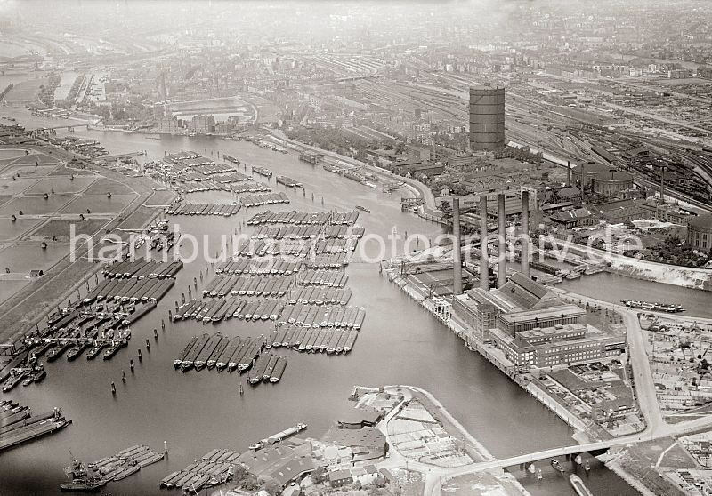 historische Fotos von der Vergangenheit Hamburgs; Luftbild des Hamburger Stadtteils. Blick ber die Billwerder Bucht, Kaltehofe - Gaswerk Rothenburgsort.  1485_0569 Luftansicht der Billwerder Bucht - dicht ankern die Binnenschiffe vor Hamburg Rothenburgsort. Im Vorder- grund rechts die Mndung vom Moorfleeter Kanal und die vier Schornsteine des Kraftwerks Tiefstack, die in das Logo der Hamburgischen Electricitts Werke HEW aufgenommen wurden. Hinter dem Kraftwerksgebude die Schleuse zum Tiefstack-Kanal und die Anlage des Gaswerks Rothenburgsort. Dahinter die Gleisanlagen des Rangierbahnhofs von Rothenburgsort. Links auf der Elbinsel Kaltehofe sind die Filterbecken der Wasserwerke zu erkennen.