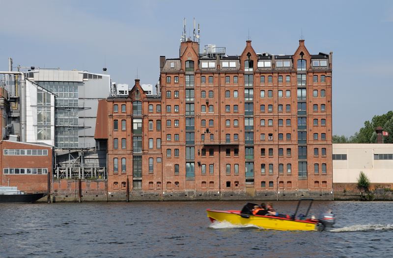 Historische Industriearchitektur - rote Ziegelfassade, Speichergebude Rothenburgsort. Fotos aus den Hamburger Stadtteilen - Rothenburgsort Bezirk Hamburg-Mitte. 1507_4770  Ein gelbes Sportboot mit Aussenbordmotor fhrt auf der Billwerder Bucht Richtung Sperrwerk. Am Ufer das historische Speichergebude mit der roten Ziegelfassade und den Tren zu den einzelnen Lagerbden.