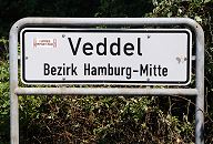 211_4274 Grenzschild des Hamburger Stadtteils Veddel, Bezirk Hamburg Mitte zu seinem nrdlichen Nachbarn Wilhelmsburg. Der Stadtteil Veddel umfasst den Ostteil der Insel Veddel sowie die Peute, ebenfalls eine Insel im Stromgebiet der Elbe. Westlich der Veddel erstreckt sich das Gebiet des Hamburger Freihafens mit dem Zollbergang am Veddeler Marktplatz. Die Veddel war ursprnglich Weideland, auf dem vorwiegend Milchwirtschaft betrieben worden istund kam durch den Gottorper Vertrag zu Hamburg.  Das alte Ortszentrum um den Veddeler Markt im Norden der Veddel war von Grnderzeit-Wohnhusern geprgt, die zumeist whrend des II. Weltkriegs zerstrt wurden - heute befindet sich dort die Autobahnanschlussstelle Hamburg-Veddel. Zwischen der Eisenbahnstrecke, die den Stadtteil nach Westen begrenzt, und der Autobahn 255 liegt ein schmales und dicht bebautes Wohnquartier. Die einzelnen Baublcke, die sich um einen zentralen Platz mit Schule gruppieren, wurden nach Plnen verschiedener Hamburger Architekten errichtet - der Rest des Stadtteils besteht vorwiegend aus Industrie- und Gewerbegebieten. Die Veddel hat eine Flche von 4,4 km und ca. 5000 Einwohner, wovon ungefhr 52% Migranten sind (Ha