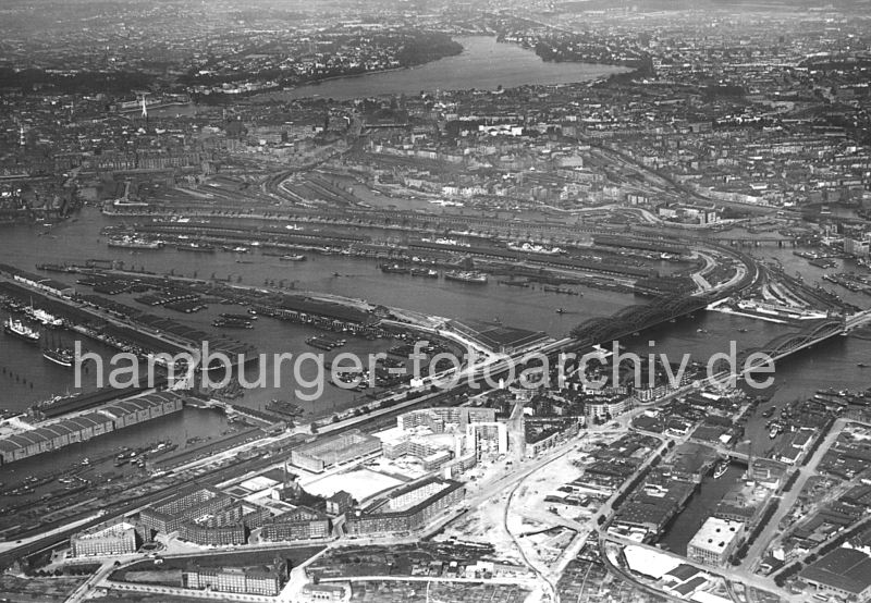 Fotografien aus den Bezirken - Hamburg Mitte, Stadtteil Veddel. Historisches Luftbild von Hamburg Veddel und dem Hamburger Hafen, ca. 1932 / Hamburg Fotografie Christoph Bellin. 212_1_2367 Luftfotografie von der Veddel und dem anschliessenden Hafengebiet - im Vordergrund die unter dem Einfluss des damaligen Oberbaudirektor Fritz Schumacher entstandenen Backstein-Wohnblocks auf der Veddel; rechts der Marktkanal, dahinter die Norderelbbrcke und die Freihafenelbbrcke ber die Norderelbe.In der Bildmitte das lange Hafenbecken des Baakenhafen, rechts der Oberhafenkanal und Billehafen. Links der Moldauhafen an dessen Stirnseite das Dresdener Ufer an der Freihafengrenze liegt; dann der Saalehafen mit den Lagerhusern am Dessauer Ufer. Darber ist noch ein Ausschnitt vom Segelschiffhafen mit dem Asiakai und Segelschiffkai zu erkennen.