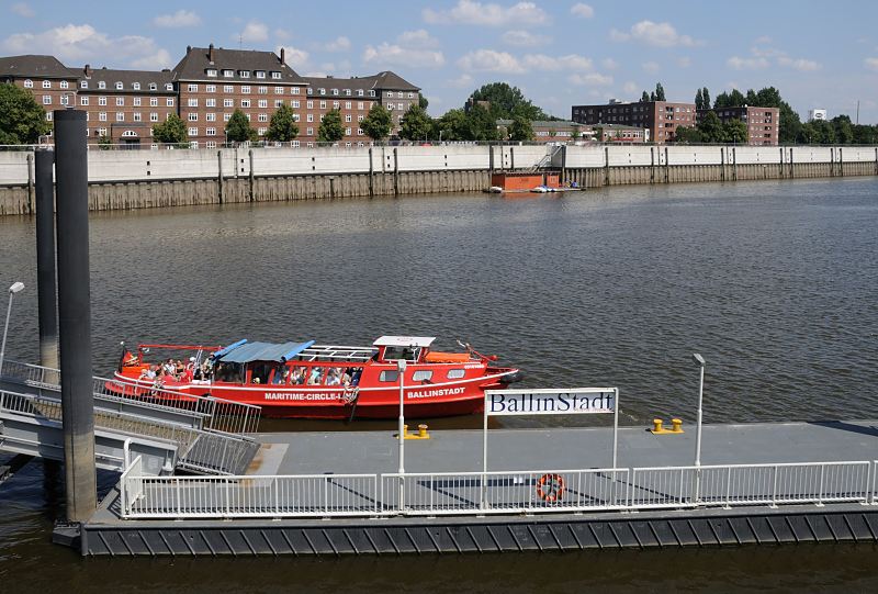 Motive aus den Hamburger Bezirken und Stadtteilen - Hamburg Veddel Anleger der Maritimen Circle Line am Mggenburger Zollhafen / Hamburger Fotografie Christoph Bellin.216_4287 Eine rote Barkasse der Maritimen Circle-Line macht gerade am Anleger Ballinstadt fest gemacht. Das Schiff ist mit Hamburg Touristen voll besetzt. Im Hintergrund die Hochwasserschutzanlage an der Promenade des Mggenburger Zollhafens - die ehemaligen Kaserne am Zollhafen (lks.) wird jetzt als Wohnraum genutzt.