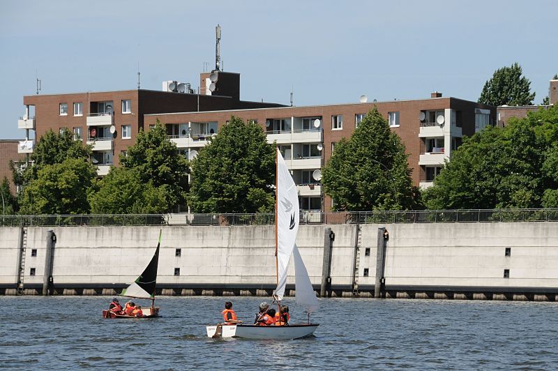 Bilder aus den Hamburger Bezirken und Stadtteilen - Hamburg Veddel Segelboote auf aum Wasser des Mggenburger Zollhafens. Hamburfotos Christoph Bellin. 217_9604 Schler und Schlerinnen der Schule Slomanstieg knnen auf dem Wasser des Mggenburger Zollhafens das Segeln lernen. Die Kinder sitzten in den Optimistenjollen und tragen signalrote Schimmwesten - am Ufer des Hafens ein Wohngebude der Veddel.