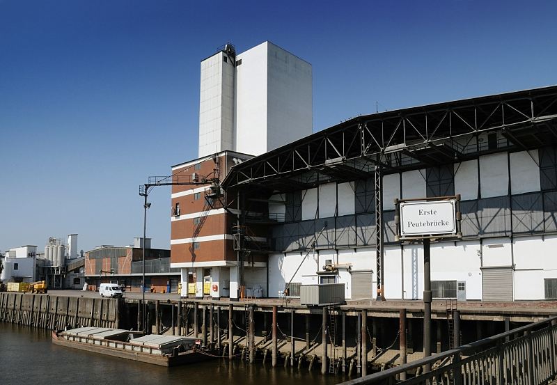 Hamburg-Bilder aus dem Bezirk Mitte, Stadtteil Veddel / Peute. Blick von der Ersten Peutebrcke auf Kaianlagen am Peutekanal.Hamburgfotograf Christoph Bellin. 228_2_4233 Die Ladung einer Schute wird gelscht - ber eine Sauganlage wird das Schttgut in den Speicher transportiert. Eisendalben vor der Kaianlage dienen zum Festmachen der Schiffe und zum Schutz des Kais.