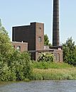 234_9505 Altes Fabrikgebäude mit hohem Ziegelschornstein am Ufer des Hovekanals. Das Ufer des Veddeler Wasserwegs ist dicht mit Schilf und Sträuchern bewachsen.