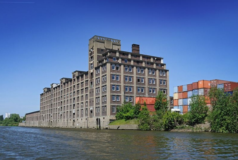 Bilder aus den Hamburger Bezirken - Bezirk Hamburg Mitte, Peute / Veddel Industriegebude, expressionistische Backsteinarchitektur - Container am Hovekanal. Fotografie Christoph Bellin. 235_9517 Expressionistisches Ziegelgebude, der ehem. Sitz der GEG am Hovekanal / Peutestrasse. Von der Norderelbe konnten die Binnenschiffe ber den Hovekanal an der Rckseite des Gebudes anlegen. Unter dem Dach sind Winden angebracht, mit denen die Waren auf die unterschiedlichen Stockwerke transportiert werden konnten. Rechts ein Stapel verschieden farbiger Container am Ufer des Kanals.