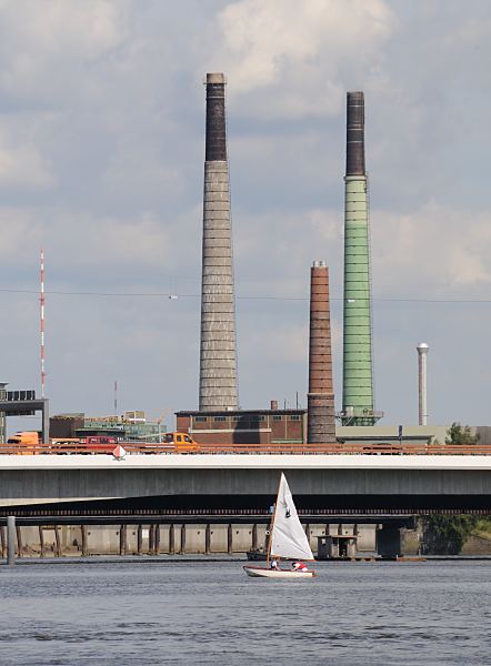 ilder aus den Stadtteilen Hamburgs Fabrikschornsteine Kupferhtte Peute, Veddel.  241_1092 Hinter der Autobahnbrcke der Bundesautobahn 255 / Abzweig Veddel die hohen Schornsteine der Kupferhtte Aurubis als Wahrzeichen des Industriegebietes auf der Peute. Ein Segelboot fhrt auf dem Wasser des Mggenburger Zollhafens - die Optimistenjolle wird von Schlern und Schlerinnen der Veddeler Schule Slomanstieg genutzt.