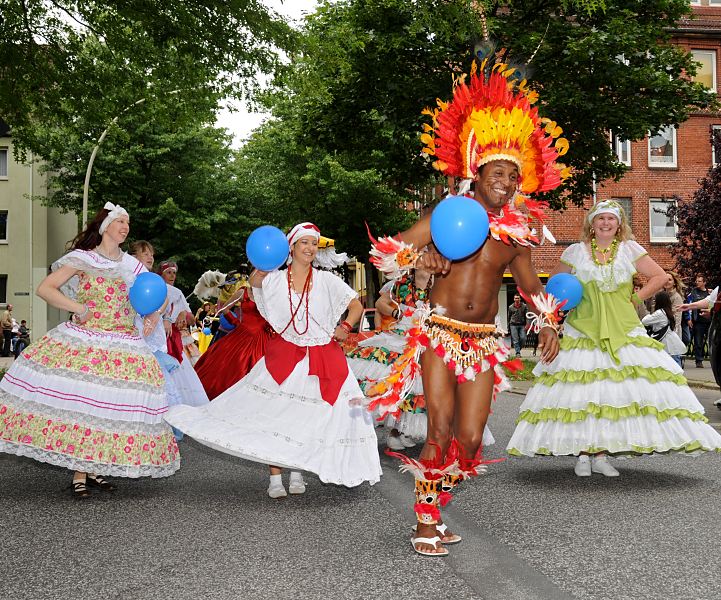 Umzug Fest der Kulturen - Tnzerin und Tnzer auf der Strasse  Hamburg-Bilder aus dem Bezirk Mitte; Stadtteil Wilhelmsburg  100_8_9942 Farbenprchtiger Umzug Fest der Kulturen - Tnzerinnen und Tnzer ziehen durch Wilhelmsburg. Der Kopfschmuck des Tnzers ist mit roten und gelben Federn geschmckt - die Tnzerinnen tragen bunte weite Kleider - sie haben ebenso wie die Zuschauer Freude ihrem Auftritt.100_8_9942 Farbenprchtiger Umzug Fest der Kulturen - Tnzerinnen und Tnzer ziehen durch Wilhelmsburg. Der Kopfschmuck des Tnzers ist mit roten und gelben Federn geschmckt - die Tnzerinnen tragen bunte weite Kleider - sie haben ebenso wie die Zuschauer Freude ihrem Auftritt.