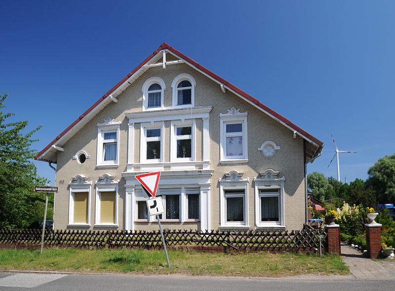 Grnderzeit Architektur, Bauernhaus - blauer Himmel ber Hamburg Fotografien aus dem Bezirk Hamburg- Mitte; Wilhelmsburg, Ortsteil Georgswerder  109_8944 Grnderzeit-Gebude am Niedergeorgswerder Deich - die Fassade des Bauernhauses ist mit gelbem Klinker verkleidet und die Fenster sind mit weissen Stuckdekoren und Sulen versehen. Im Hintergrund ein Windrad der Windkraftanlage Georgswerder. www.bilder-hamburg.de