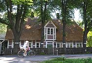 110_9321 Strohdachhaus in Hamburg-Georgswerder; die Fachwerkbalken des historischen Gebudes sind weiss gestrichen und die Fachwerk-Zwischenrume mit rotem Klinker gefllt. Hohe Linden stehen vor dem Haus, eine Fahrradfahrerin fhrt auf der Strasse. www.bilder-hamburg.de