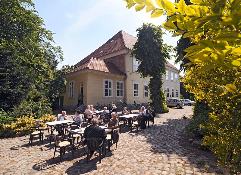 Fotos aus dem Hamburger Bezirk Mitte, Stadtteil Wilhelmsburg - Ortsteil Kirchdorf  119_9110 Das Museum Elbinsel Wilhelmsburg hat seinen Sitz im alten Hannoversche Amtshaus. In seinen Rumen zeigt das Regional-Museum die Geschichte und buerliche Kultur Wilhelmsburgs. In dem Museumscaf sitzen Gste auf dem Kopfsteinpflaster vor dem Museumsgebude im Freien. www.fotos-hamburg.de