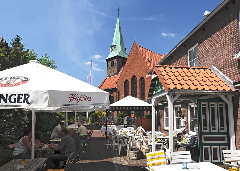 Fotos aus dem Bezirk Hamburg-Mitte, Elbinsel Wilhelmsburg / Kirchdorf  122_9098 Die evangelisch lutherische Kreuzkirche in Hamburg Kirchdorf bildet den historischen Kern von Wilhelmsburg;  die Fachwerk-Saal-Kirche entstand 1614 und ist Ziel von Fahrradtouren und Wanderausflgen auf der Elbinsel Wilhelmsburg. Ausflgler machen Rast in dem Caf vor der Kirche - sie sitzen unter Sonnenschirmen auf dem Vorplatz. www.fotos-hamburg.de