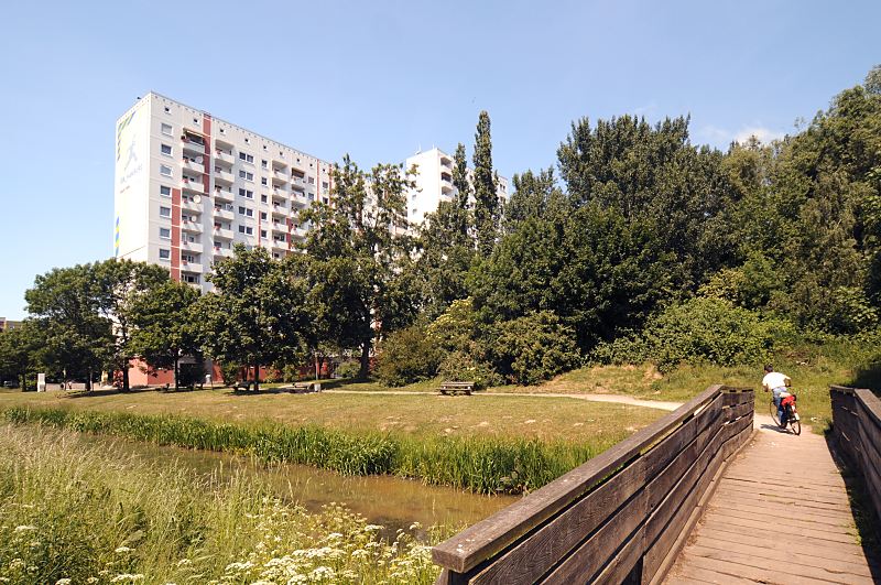 Fotos aus Hamburg - Mitte, Stadtteil Wilhelmsburg Ortsteil Kirchdorf Sd. 128_9036 Blick ber den Brausielgraben zu einem Hochhaus in der Wohnanlage Kirchdorf-Sd. Bnke stehen an der Wiese. Ein Junge fhrt mit seinem Fahrrad ber eine Holzbrcke, die ber den Brausielgraben fhrt. www.fotos- hamburg.de