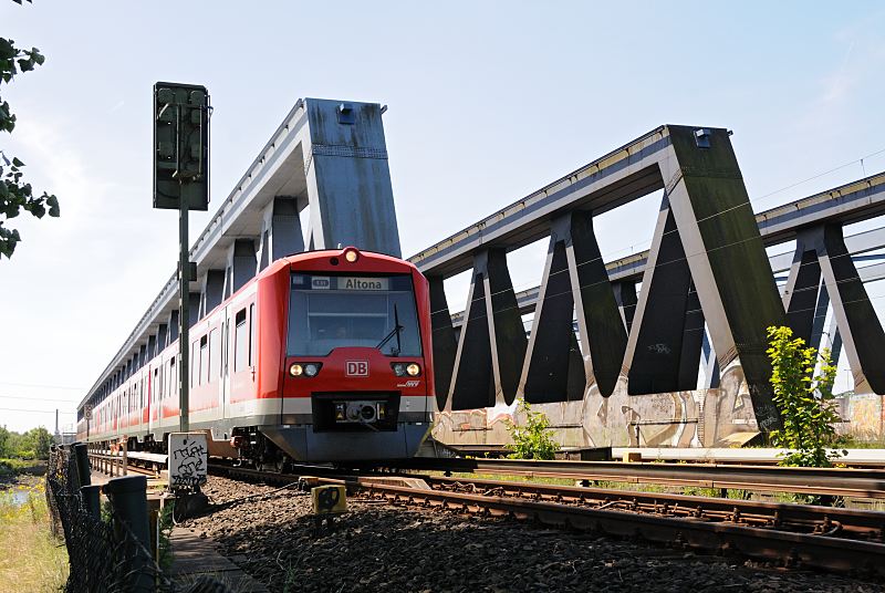 Eisenbahnbrcke ber die Sderelbe; S-Bahn-Zug Richtung Hamburg Altona Hamburgbilder aus dem Bezirk Mitte; Sderelbe bei Wilhelmsburg Stillhorn 155_0971  Seit 1872 berquerte die Bahn die Sderelbe ber eine Bogenbrcke; diese wurde 1970 abgerisschen und durch dei 340m lange Fachwerkbrcke ersetzt. Ein roter Zug der Hamburger S-Bahn kommt aus Harburg und fhrt Richtung Hamburg Altona.