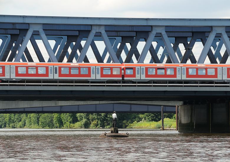 Hamburgfotos aus den Bezriken; Hamburg-Mitte; Sderelbe bei Wilhelmsburg Eisenbahnbrcke ber die Sderelbe; S-Bahn-Zug  156_0751  Die erste Eisenbahnbrcke ber die Sderelbe wurde 1872 errichtet; diese wurde 1970 abgerissen und durch dei 340m lange Fachwerkbrcke ersetzt. Ein roter Zug der Hamburger S-Bahn kommt aus Harburg und fhrt Richtung Hamburg Altona. Bei der Brcke schwimmt einer der "Vier Mnner auf Bojen", die als Teil eines Kunstwerks im ffentlichen Raum auf der Alster, Bille und Elbe zu finden sind ( weitere: Alster/Schwanenwik; Elbe/Strandperle; Bille/Bergedorfer Hafen)