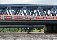 156_0751  Die erste Eisenbahnbrcke ber die Sderelbe wurde 1872 errichtet; diese wurde 1970 abgerissen und durch dei 340m lange Fachwerkbrcke ersetzt. Ein roter Zug der Hamburger S-Bahn kommt aus Harburg und fhrt Richtung Hamburg Altona. Bei der Brcke schwimmt einer der "Vier Mnner auf Bojen", die als Teil eines Kunstwerks im ffentlichen Raum auf der Alster, Bille und Elbe zu finden sind ( weitere: Alster/Schwanenwik; Elbe/Strandperle; Bille/Bergedorfer Hafen)