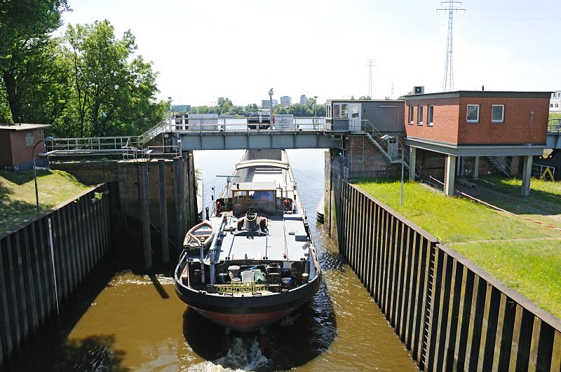 Fotografien aus dem Hamburger Bezirk Mitte - Stadteil Wilhelmsburg / Reiherstieg  Binnenschiff in der Reiherstiegschleuse - Ausfahrt zur Sderelbe  160_0930  Ein Binnenschiff hat seine Fracht im Hamburger Hafen gelscht und fhrt ohne Ladung durch das geffnete Schleusentor der Reiherstiegschleuse in die Sderelbe. Rechts das ehem. Schleusenwrterhaus; die Schlickschleuse am Reiherstieg wird ferngesteuert - ein Radar erfasst die ankommenden Schiffe. Auf der gegenberliegenden Seite der Sderelbe sind die ehem. Silobauten und Fabrikgebude des Harburger Hafens zu erkennen.