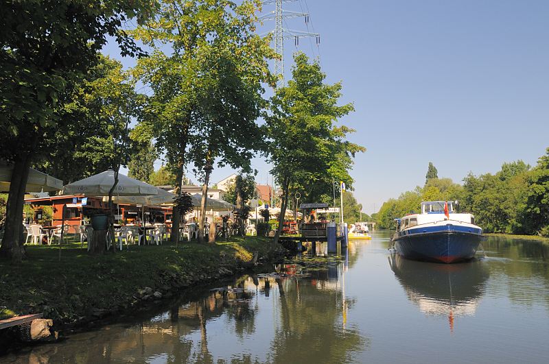 Fotografien aus den Bezirken -  Hamburg Mitte, Stadtteil Wilhelmsburg  Anleger Ernst-August-Kanal, Biergarten mit Sonnenschirmen, Barkasse  57_9229 Biergarten am Ufer des Ernst-August-Kanals; Sonnenschirme und Tische stehem auf der Wiese am Wasser. Eine Barkasse der Wilhelmsburg- und Hafenrundfahrt hat am frhen Vormittag vom Anleger abgelegt. www.fotograf- hamburg.com