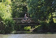 72_8773 Ein Fahrradfahrer fährt über eine Holzbrücke entlang des Wanderweges am Ufer des Assmannkanals. Das Kanalufer ist mit Bäumen und Büschen dicht bewachsen.  Der Aßmann- kanal ist ein Seitenkanal des Ernst- August- Kanals und wurde 1929 gegraben. Es ist geplant, den Kanallauf bis zur Menge- strasse zu verlängern. ©www.fotograf- hamburg.de