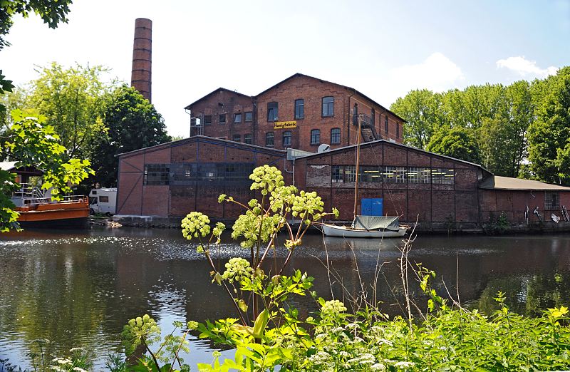 Fotos aus dem Bezirk Hamburg Mitte - Stadtteil Hamburg-Wilhelmsburg Veringkanal, Industriegebude Kulturzentrum Honigfabrik 74_9430 Blick ber den Veringkanal zum Industriegebude mit hohem Schornstein, das 1906 errichtet wurde. Die Fabrikanlage wurde zum Honigschleudern / Honigabfllung und auch als Margarinefabrik genutzt. Jetzt hat das Kulturzentrum Honigfabrik dort seinen Sitz. www.fotograf- hamburg.de