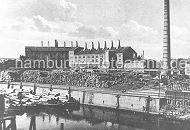 79_0247 Historisches Foto aus Hamburg Wilhelmsburg ca. 1920 - am Ufer des Veringkanals sind Baumstämme gestapelt; an den Kaianlagen liegen Schuten, die ebenfalls hoch mit Baumstämmen beladen sind. Im Hintergrund Fabrikgebäude und Schornsteine.  www.hamburger-fotoarchiv.de