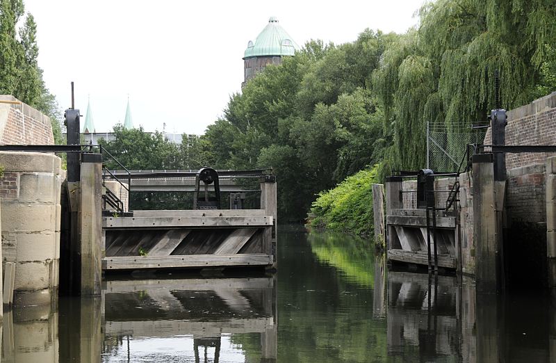 historische Schleuse am Veringkanal - Schleusentore aus Holz, Wasserturm  Hamburg-Fotografien aus dem Stadtteil Wilhelmsburg, Bezirk Hamburg-Mitte  83_7342 Eines der Holztore der historischen Veringkanal-Schleuse ist geffnet - die Schleuse wurde 1896 errichtet und wird von Hand betrieben. Die Anlage wurde 2008 restauriert. Weiden stehen am Ufer des Kanals - im Hintergrund die Kuppel vom Wilhelmsburger Wasserturm und die Spitzen der Kirchtrme dSt. Bonifatius-Kirche. www.fotograf- hamburg.de