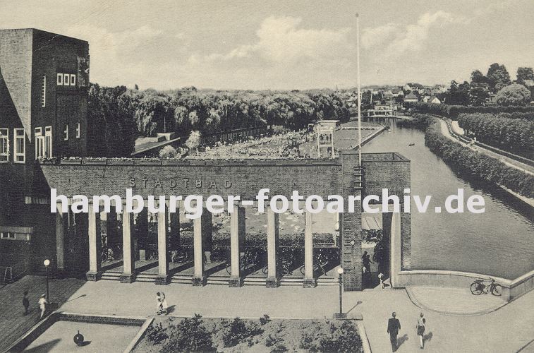 alte Hamburg Fotos - Bergedorfer Billebad / Stadtbad; Freibad am Hamburger Fluss Bille -- 11_21549 alte Fotografie vom Bergedorfer Stadtbad ca. 1930; das Freibad liegt direkt an der Bille. Im Hintergrund sind die Schwimmbecken zu erkennen, dicht gedrngt liegen und sitzen die Badegste bei sonnigem Wetter in der Badanstalt am Wasser. Im Vordergrund die Backstein-Architektur vom Eingangsgebude des Bille-Bads - im Eingangsbereich mit den hohen Sulen stehen die Fahrrder der Badegste. Rechts fhrt eine Fussgnger Brcke ber die Bille zum Schillerufer.  www.hamburger-fotoarchiv.de