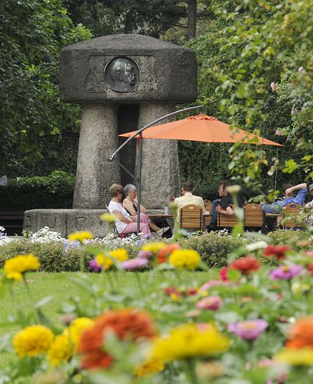 Foto Bismarck Denkmal Bilder Bergedorfer Schlosspark  11_21557 Das Bergedorfer Bismarck Denkmal wurde 1906 eingeweiht, den Entwurf fr die monumentale Erinnerungssttte lieferte Karl Garbers. Das Bismarkdenkmal wurde 1906 eingeweiht -  erst spter wurde es in den Bergedorfer Schlosspark versetzt. Im Vordergrund blhen bunte Blumen - Parkbesucher sitzen unter einem Sonnenschirm in einem Caf neben dem Granitdenkmal an dessen Stirnseite die Kupferplakette mit dem Kopf Bismarcks. www.hamburg-fotograf.com