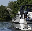 11_21582 Das weisse Motorboot fhrt in der Flussmitte der Dove- Elbe; der Freizeitkapitn steht am Steuerstand unter der Persenning als Schutz gegen die Sonne. Hinter dem Deich ist das Strohdach eines Wohnhauses zu erkennen. www.hamburg-fotograf.com