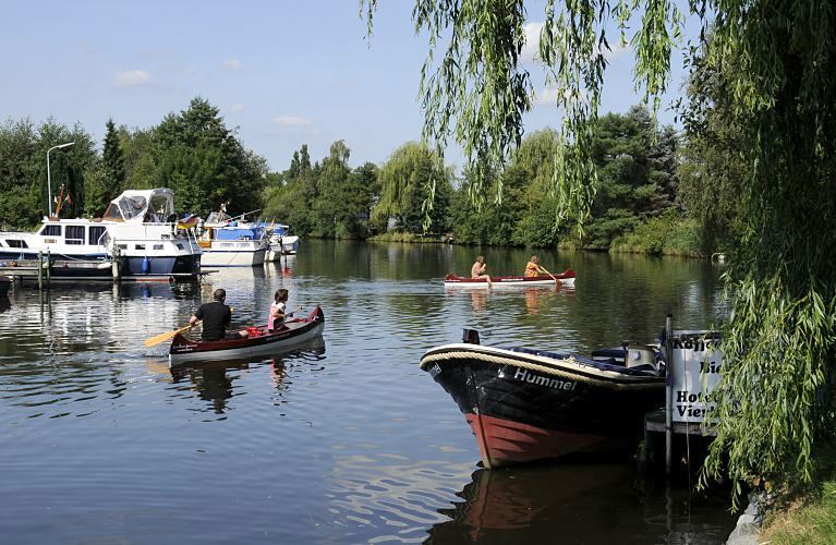 Hamburg Fotograf - Motive der Flsse Hamburgs - Kanus und Yachthafen an der Dove-Elbe   11_21584 Zwei Kanus fahren bei strahlendem Hamburger Sommerwetter auf der Dove-Elbe - lks. linken liegen Motoryachten am Bootssteg eines Vierlnder Yachthafens. Im Vordergrund am Steg des Hotels Vierlande hat das Tuckerboot HUMMEL festgemacht - ein dicker umlaufenden Tampen / Seil dient als Scheuerschutz. Die Tuckerboote waren offene Arbeitsbarkassen im Hamburger Hafen; sie brachten als Zubringerboote u.a. auch Hafenarbeiter an ihren Arbeitsplatz. www.hamburg-fotos.org 