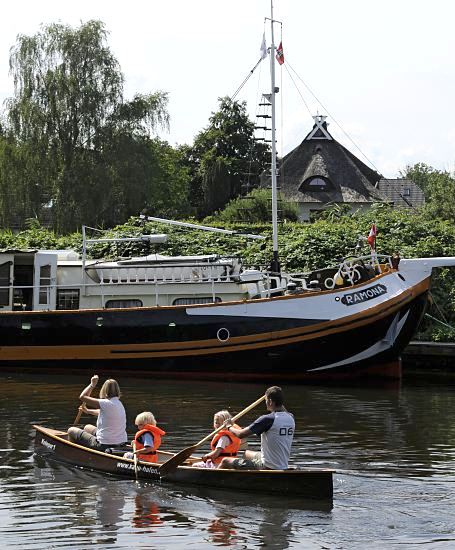 Hamburger Fotografien - Sommer in Hamburg   11_21585 Eine Familie paddeln in einem Kanu auf der Dove-Elbe - die Kinder tragen zur Sicherheit Schwimmwesten. Am Ufer liegt ein Segelschiff, das zum Hausboot umgebaut wurde. Im Hintergrund ein strohgedecktes Wohnhaus. www.hamburg-fotos.org 