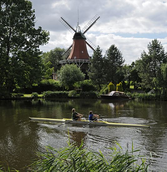 Bilder Hamburger Wassersport -  Dove-Elbe, Reitbrooker Mhle  11_21594 Die Dove-Elbe ist ein beliebtes Hamburger Gewsser fr den Bootssport. Ein Ruderboot fhrt in der Sonne auf der Doveelbe - der Doppelzweier hat gerade die Reitbrooker Mhlenbrcke passiert und kommt an der historische Reitbrooker Windmhle vorbei. Die Kornmhle wurde  ursprnglich 1773 errichtet und nach einem Brand 1870 neu erbaut. Am Ufer im Vordergrund wchst dichtes Schilf - auf der anderen Uferseite liegt am Bootsanleger ein kleines Sportboot.  www.hamburg-fotos.org